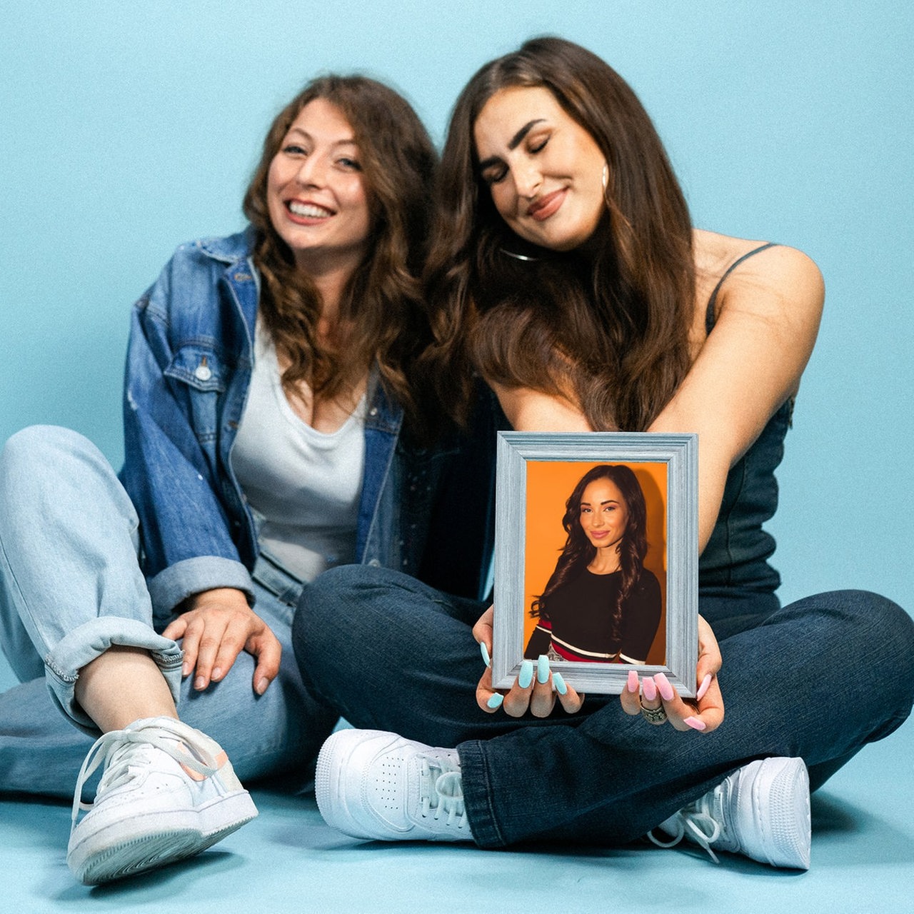 Karina und Larissa sitzen auf dem Boden und halten ein Porträt in der Hand.